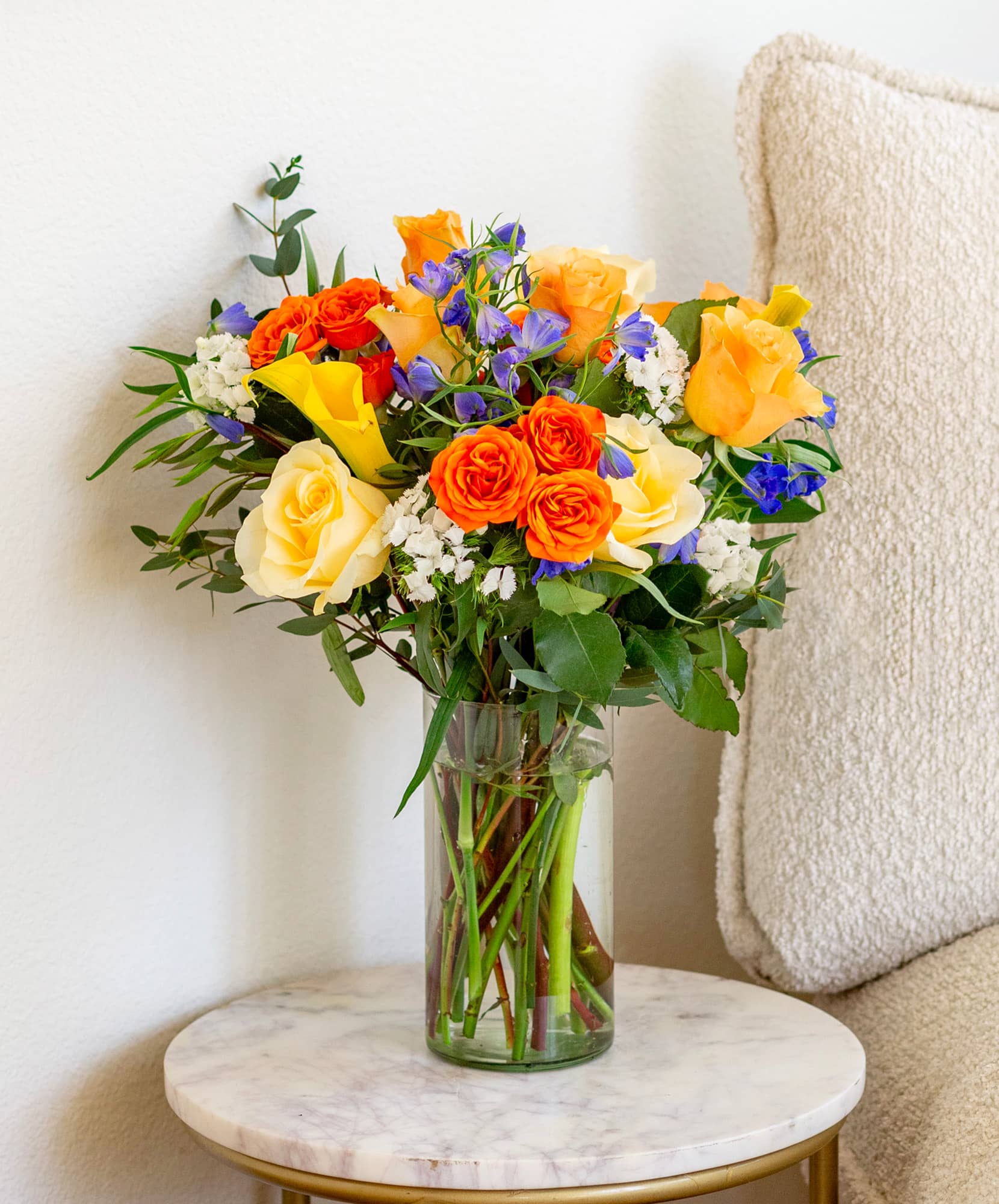 Vibrant bouquet of orange and yellow roses with blue accents, perfect for brightening up any space.