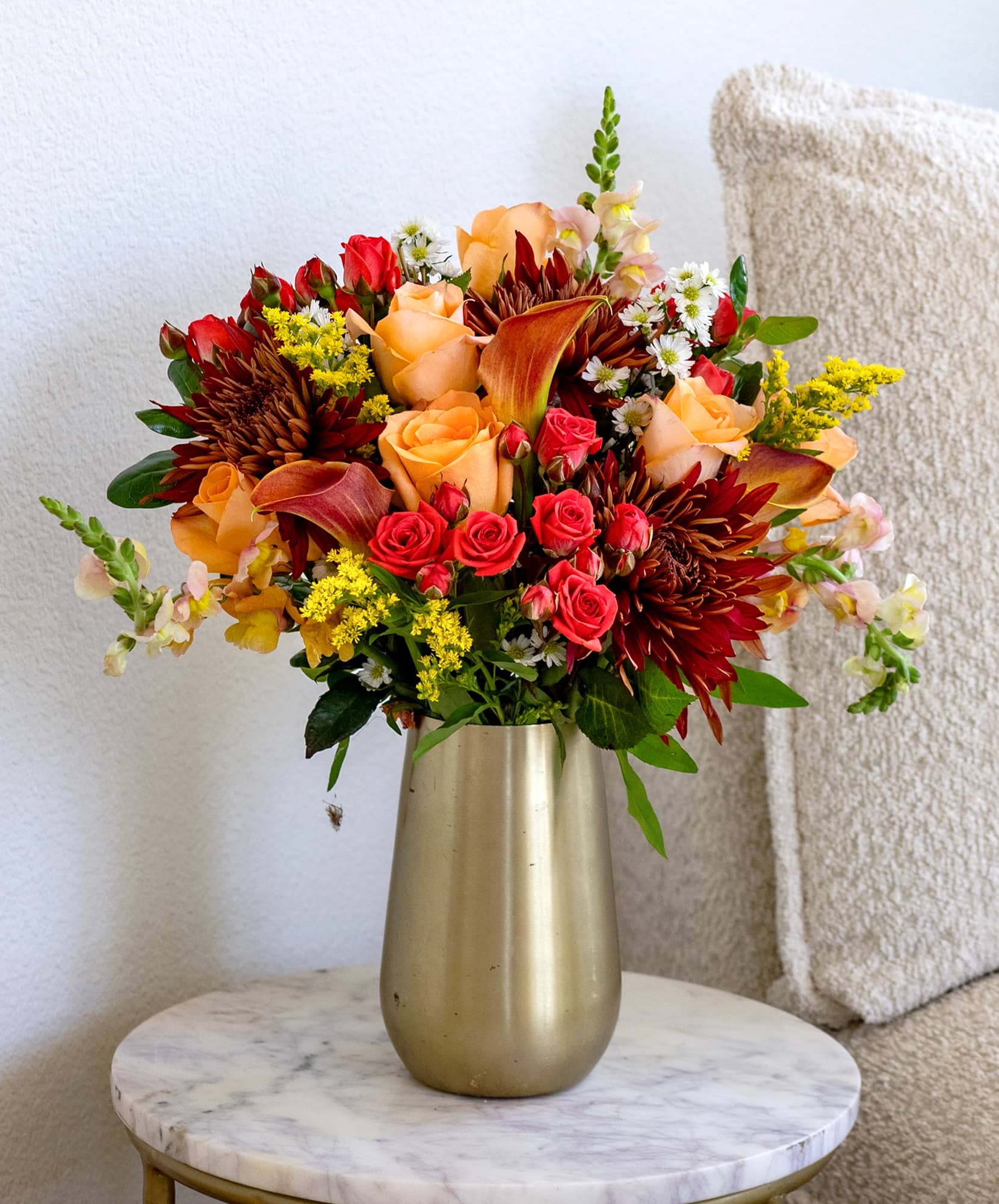 Vibrant floral arrangement with orange roses, yellow blooms, and seasonal accents.